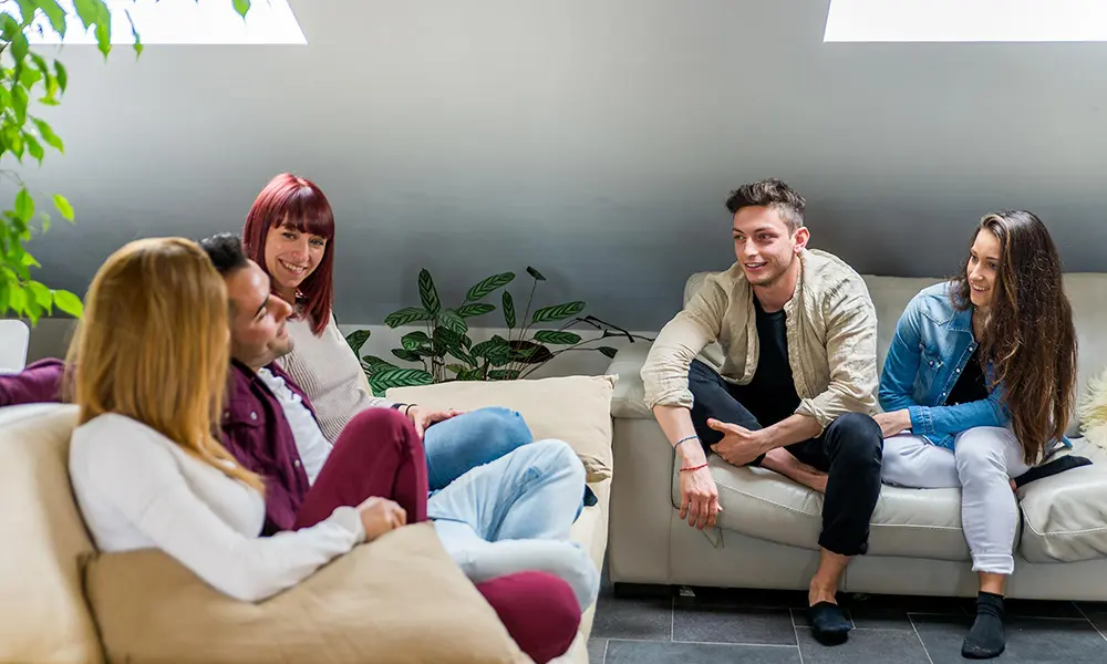 Young adults relaxing and talking together on couches in a sober living home